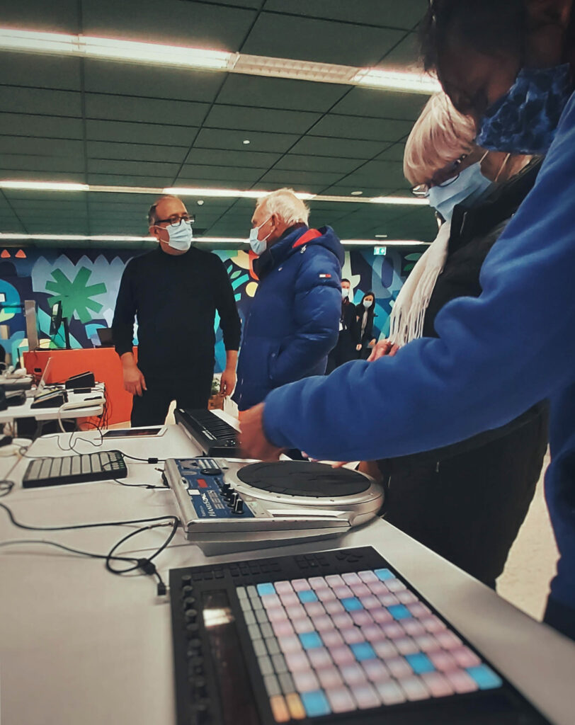 Two tutors, Nikos and Elvy show electronic instruments to an elderly couple, at 2 Royal Ave in Belfast.