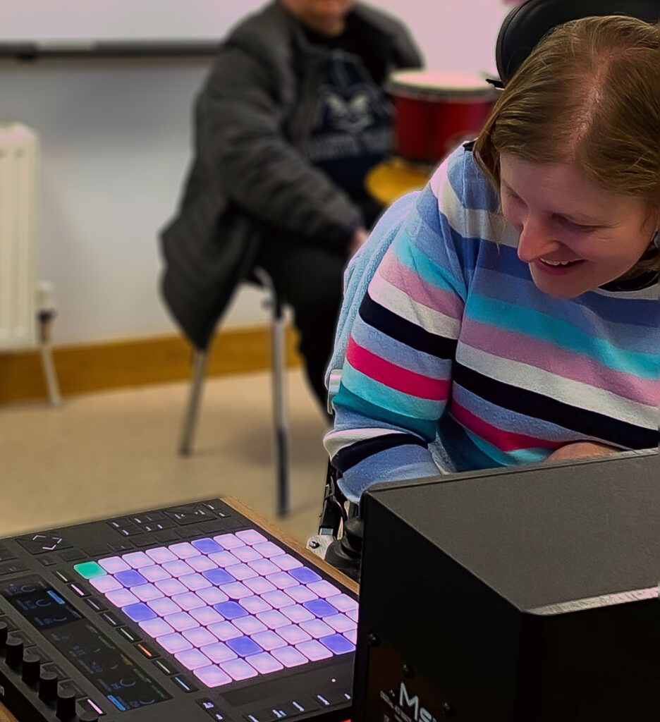 Participant Claire smiles while playing the Ableton Push 2 during the Brain Injury Matters workshop session in Belfast.