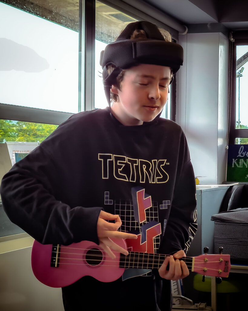 Young man plays the ukulele with his eyes closed during Drake's workshopt at Goal Line, Portadown