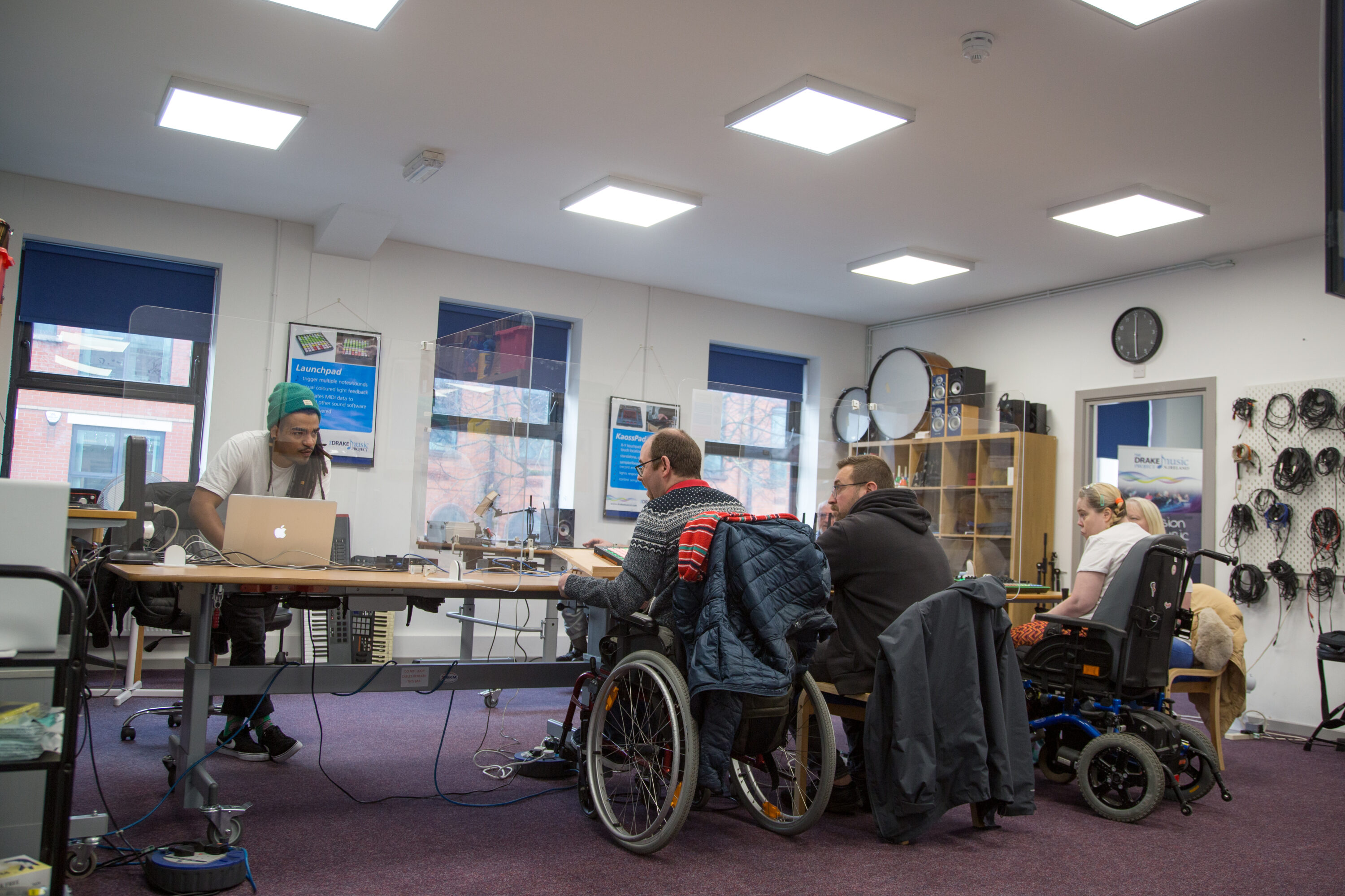 Wide shot of the two musicians,Tim and Marylouise, accompained by their family member Chirs and Michelle. They all look attentive to the tutor Henrique during a  
Wired Ensemble Session at Drake Belfast's studio.