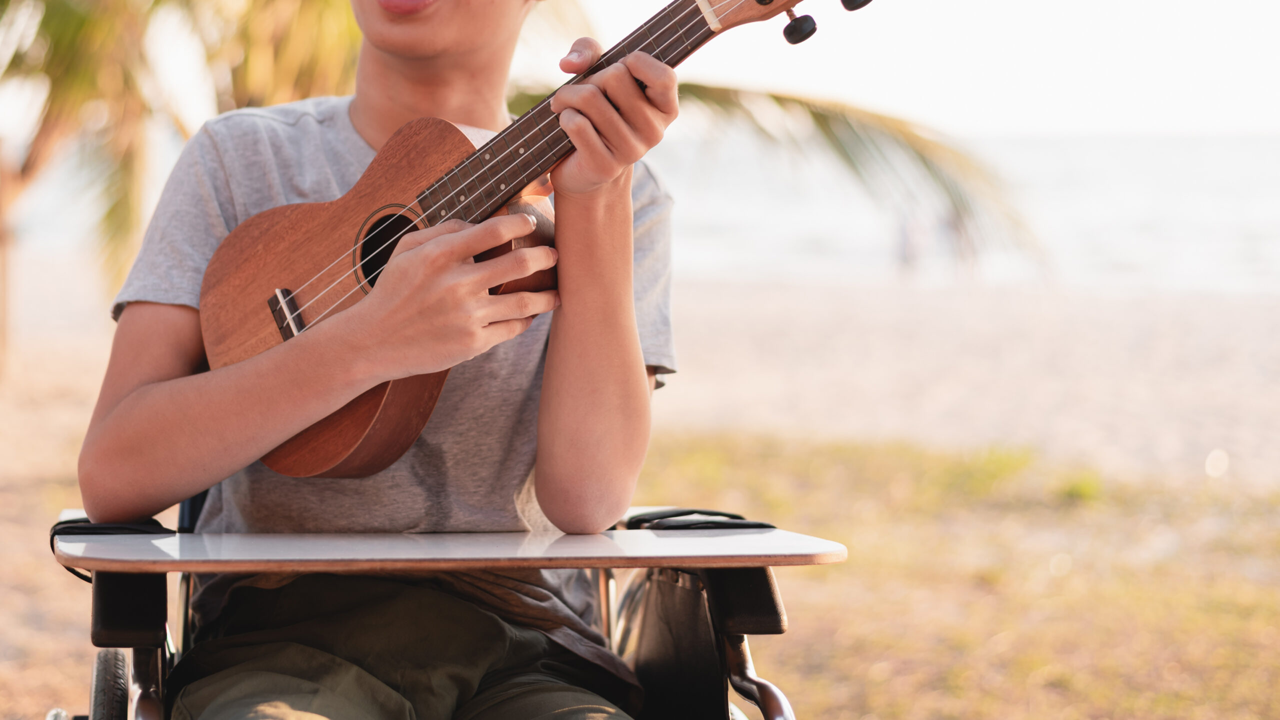 Close-up of a young man in a wheelchair playing the ukulele at the beach